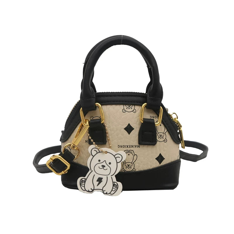 Black and beige handbag with gold accents and a teddy bear charm on a white background